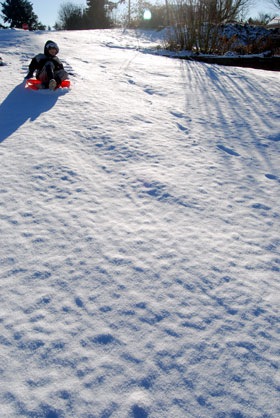 boy sledding on new snow hill at winter sunrise