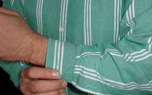 Man buttoning cuff on green striped mens shirt